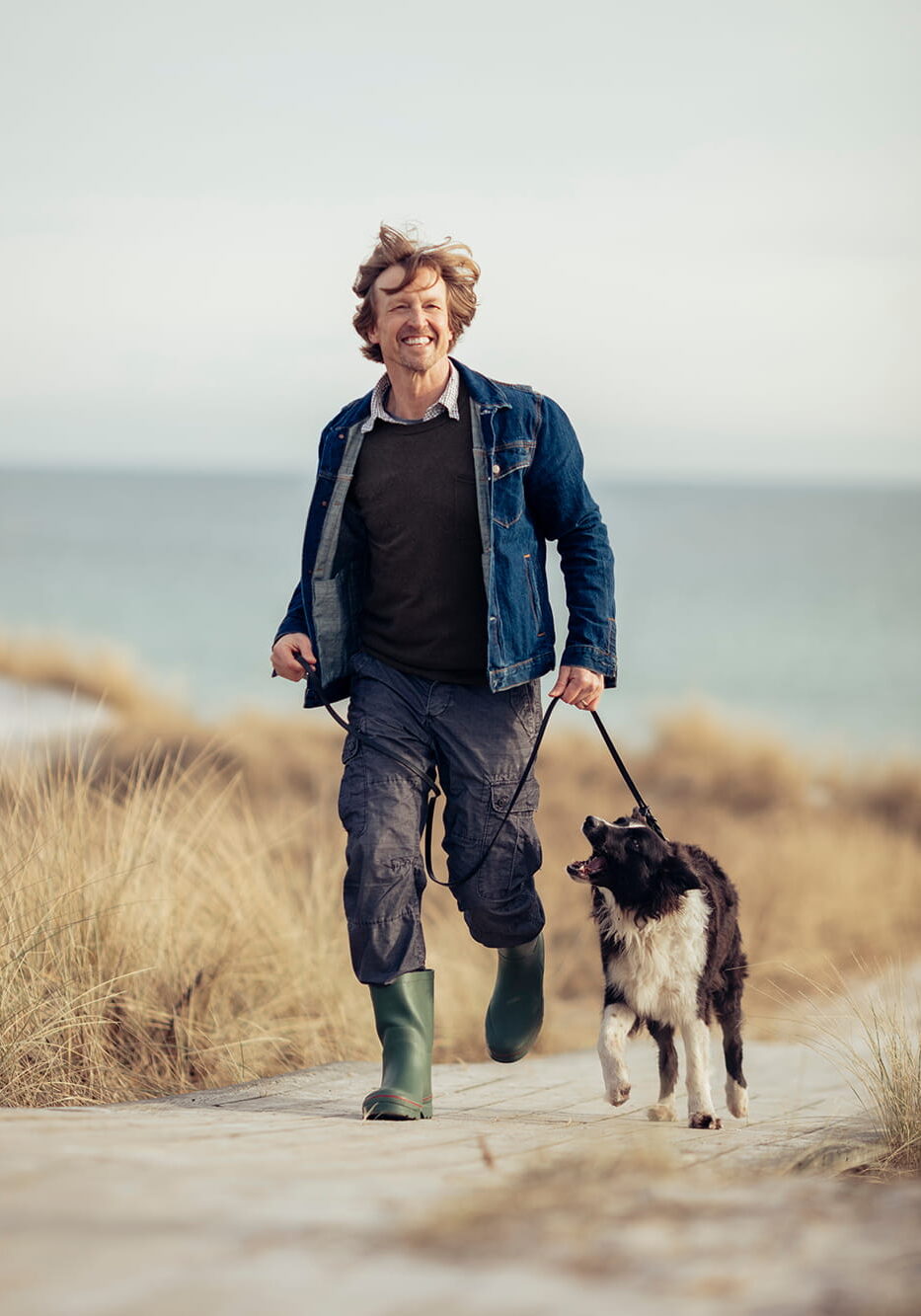 A middle aged man walking his dog on the beach